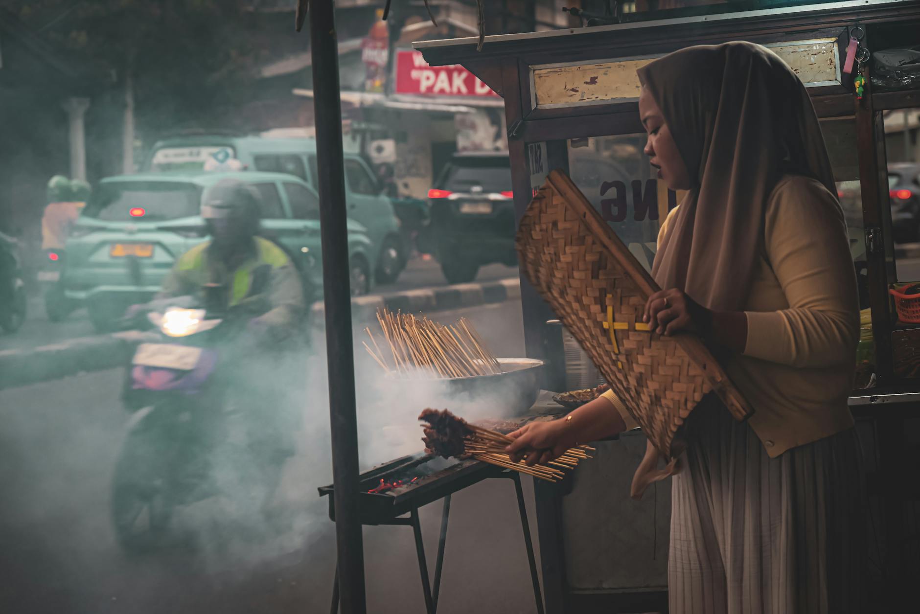 Kobieta grilluje szaszłyki satay w ulicznej budce w Dżakarcie wieczorem Kobieta grilluje szaszłyki satay w ulicznej budce w Dżakarcie wieczorem